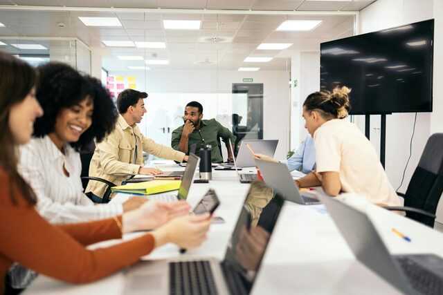 Team of five colleagues collaborating around a table with laptops in a conference room