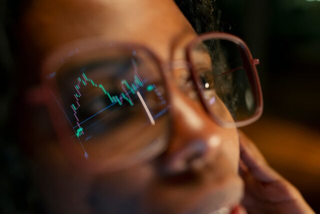 Close-up of eyeglasses reflecting a green candlestick trading chart